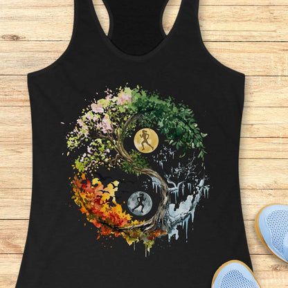 A black racerback tank top laid flat on a light wood surface, featuring a large multicolor Yin Yang graphic with a running figure and autumn leaves. Partial blue sneakers are visible at the bottom right as styling props.