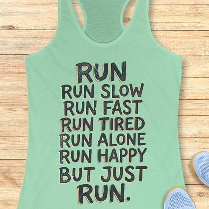 A mint green racerback tank top with a motivational quote printed in black block letters, laid flat on a light wood background with blue sneakers partially visible in the corner.