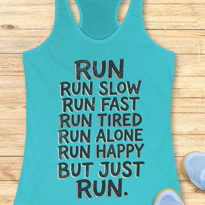 A turquoise racerback tank top with black text reading 'RUN RUN SLOW RUN FAST RUN TIRED RUN ALONE RUN HAPPY BUT JUST RUN.' laid flat on a light wood background, with partial sneakers visible at the edges.