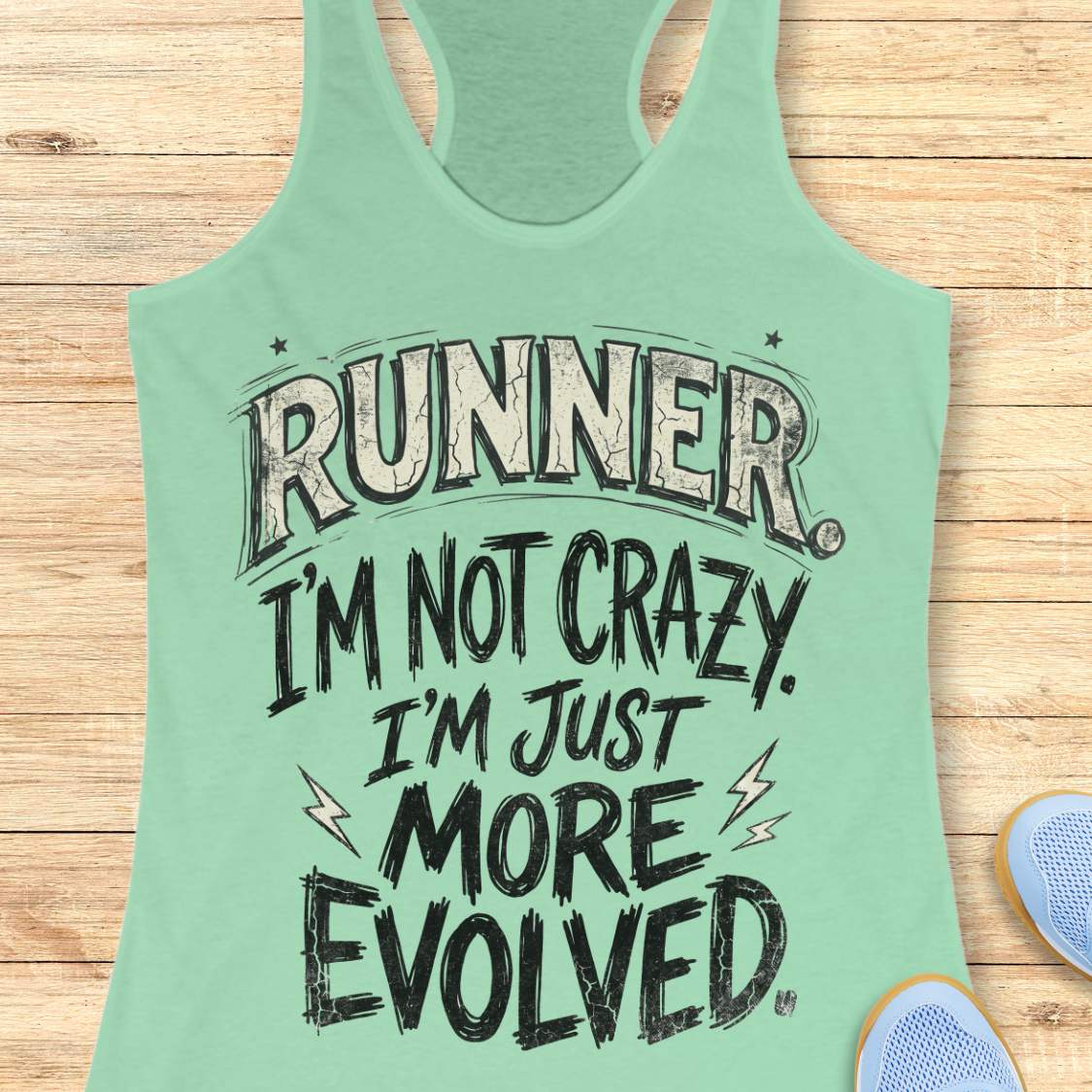 A mint green racerback tank top with a humorous graphic text reading 'RUNNER I'M NOT CRAZY. I'M JUST MORE EVOLVED.