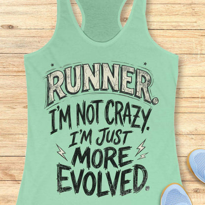 A mint green racerback tank top with a humorous graphic text reading 'RUNNER I'M NOT CRAZY. I'M JUST MORE EVOLVED.