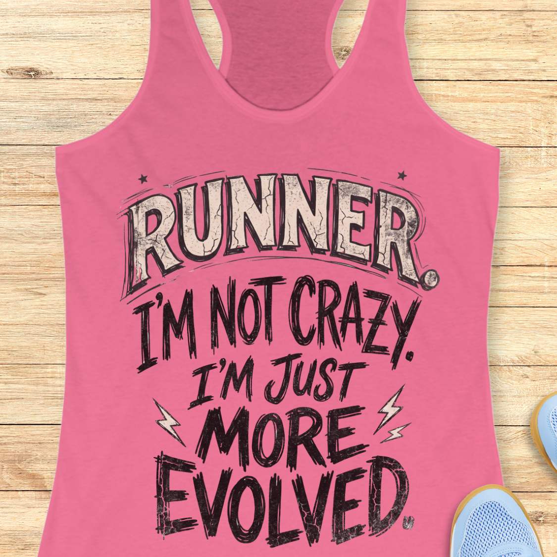 A pink racerback tank top laid flat on a light wood background, featuring the text 'RUNNER. I'M NOT CRAZY.