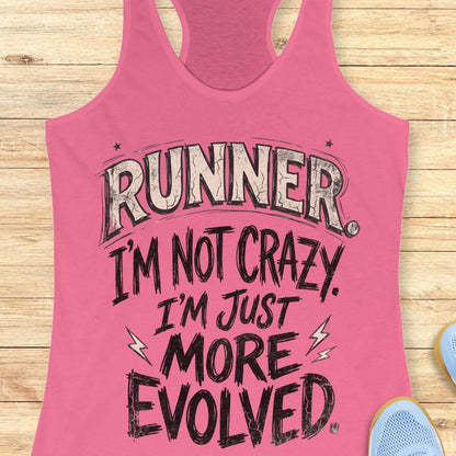 A pink racerback tank top laid flat on a light wood background, featuring the text 'RUNNER. I'M NOT CRAZY.