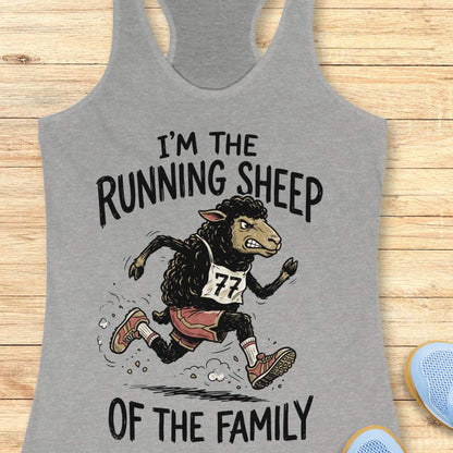 A heather gray racerback tank top laid flat on a light wood surface, featuring a graphic of a cartoon running sheep wearing a race bib numbered 77, with the text 'I'M THE RUNNING SHEEP OF THE FAMILY'.