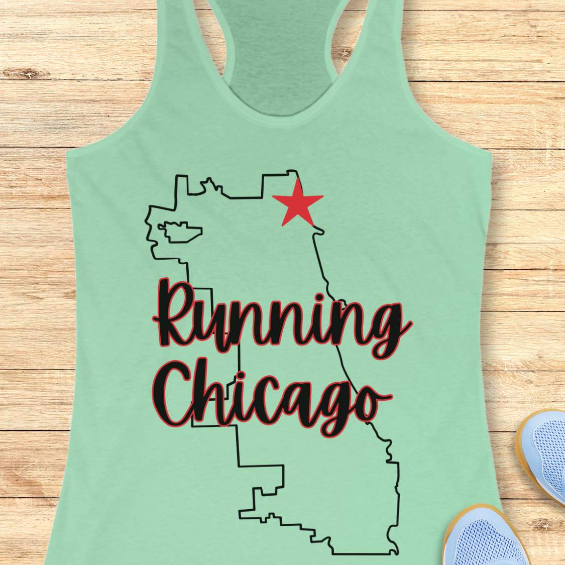 mint racerback running tank top featuring a minimalist white outline of the city of Chicago. A large red six-pointed star, inspired by the Chicago flag, marks a location near the upper right section of the city outline. The words “Running Chicago” appear in large script lettering layered over the map design. The tank top is displayed on a light wood background with partial blue running shoes visible in the bottom corners. The design has a clean, modern look celebrating running in Chicago.