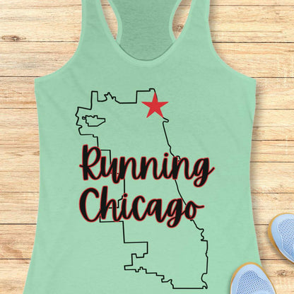 mint racerback running tank top featuring a minimalist white outline of the city of Chicago. A large red six-pointed star, inspired by the Chicago flag, marks a location near the upper right section of the city outline. The words “Running Chicago” appear in large script lettering layered over the map design. The tank top is displayed on a light wood background with partial blue running shoes visible in the bottom corners. The design has a clean, modern look celebrating running in Chicago.
