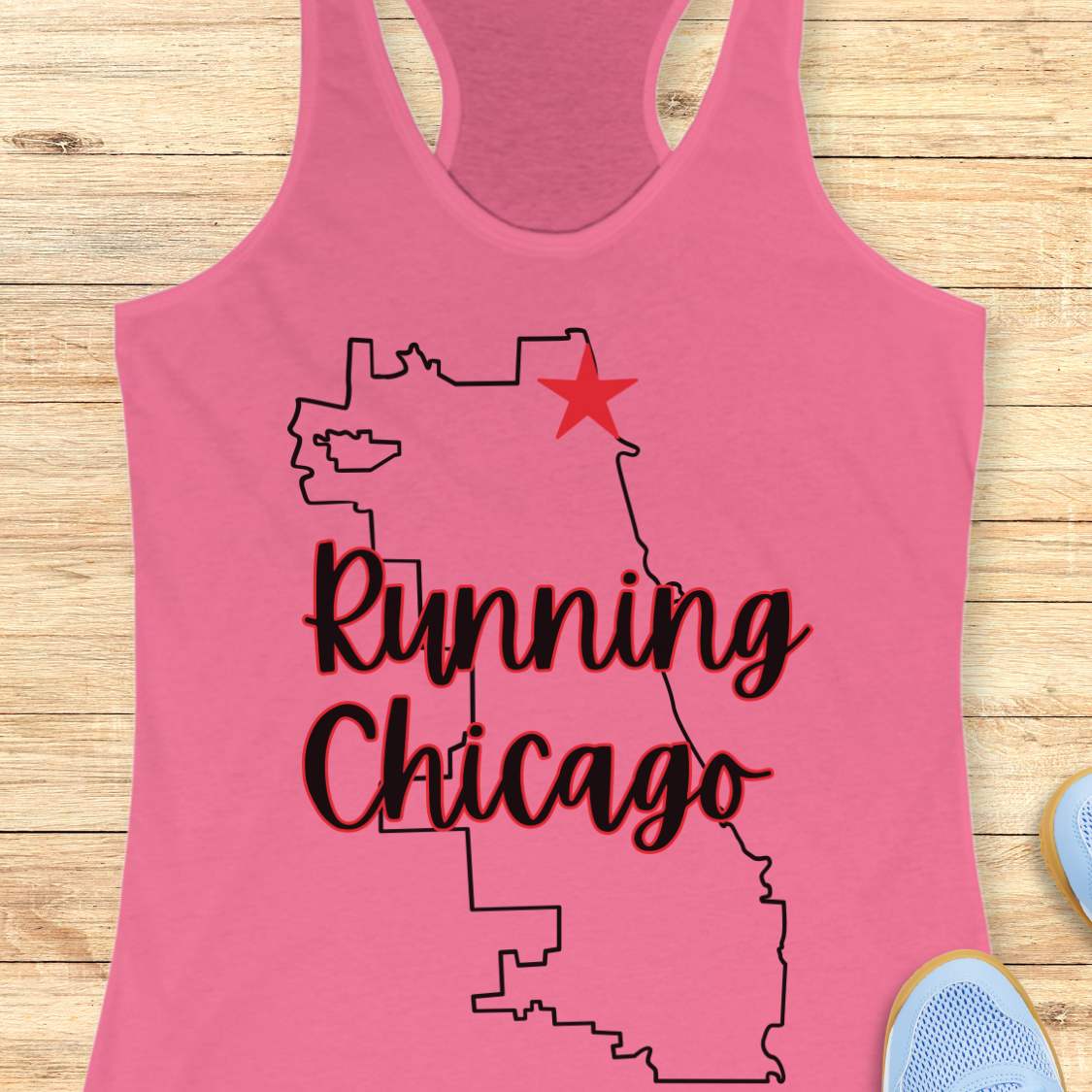 pink racerback running tank top featuring a minimalist white outline of the city of Chicago. A large red six-pointed star, inspired by the Chicago flag, marks a location near the upper right section of the city outline. The words “Running Chicago” appear in large script lettering layered over the map design. The tank top is displayed on a light wood background with partial blue running shoes visible in the bottom corners. The design has a clean, modern look celebrating running in Chicago.