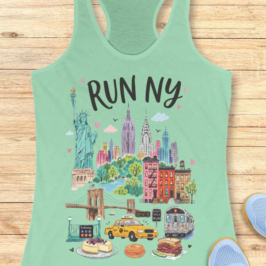 mint racerback running tank top featuring a colorful illustrated “RUN NY” design. The artwork showcases iconic New York City landmarks and symbols, including the Statue of Liberty, the Empire State Building, the Chrysler Building, the Brooklyn Bridge, brownstone row houses, a subway train, and a subway entrance. Additional New York elements include a yellow taxi cab, a race clock, a pedestrian crossing sign that reads “DON'T WALK RUN,” Central Park-inspired greenery, cheesecake, a bagel sandwich, and a pas