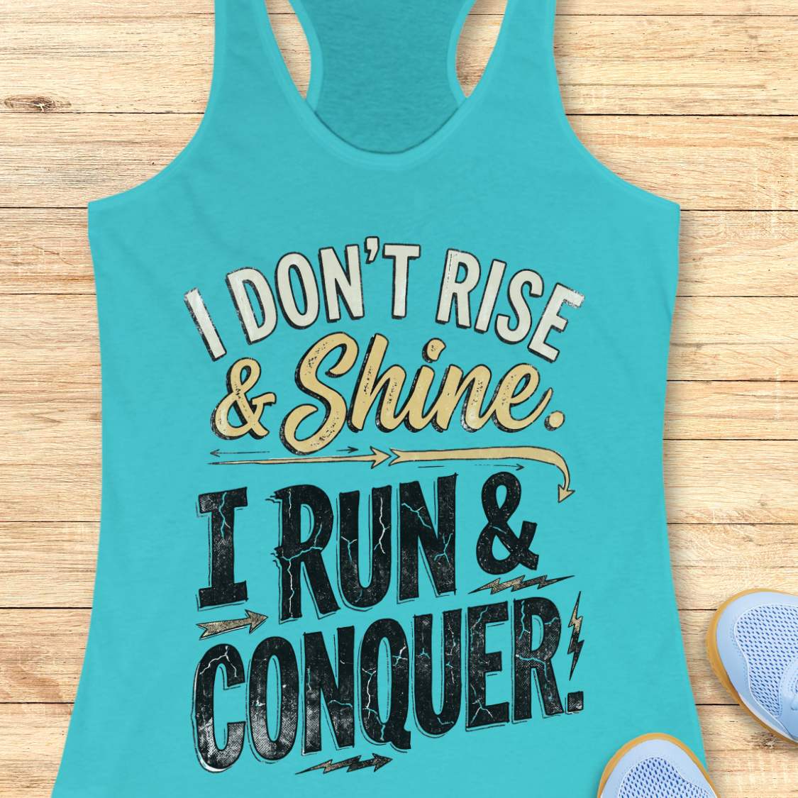 blue racerback running tank top displayed on a light wood background, featuring a distressed vintage-style graphic with blue and white lettering that reads: “I DON’T RISE & SHINE. I RUN & CONQUER.” Decorative arrows and lightning bolt accents surround the text. Partial blue running shoes are visible in the bottom corners of the image.