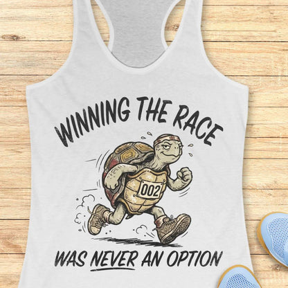 White racerback running tank top displayed on a light wood background, featuring a vintage-style illustration of a turtle running in sneakers and wearing a race bib numbered “002.” The design includes the humorous slogan: “WINNING THE RACE WAS NEVER AN OPTION.” Partial blue running shoes are visible in the bottom corners of the image.