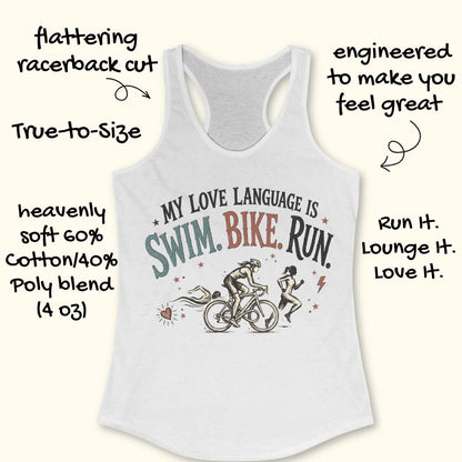 White racerback tank top displayed on a light wood background, featuring a vintage-inspired triathlon design with illustrations of a swimmer, cyclist, and runner. The graphic includes colorful distressed lettering that reads: “MY LOVE LANGUAGE IS SWIM. BIKE. RUN.” Small decorative stars, a heart, and a lightning bolt accent the design. Partial blue running shoes are visible in the bottom corners of the image.