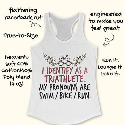 A white racerback tank top with a triathlete graphic and text, shown on a light beige background with decorative handwritten callouts around it. The graphic includes wings, glasses, a bicycle, and the text 'I IDENTIFY AS A TRIATHLETE.