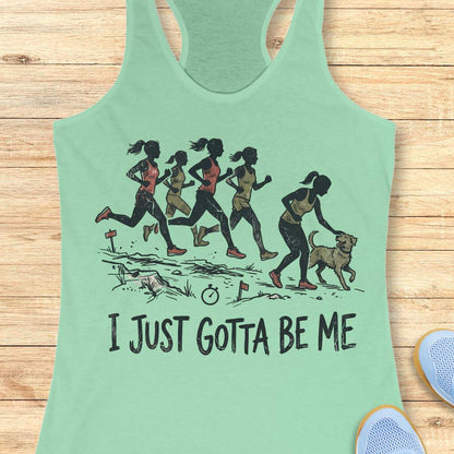 mint racerback tank top featuring a distressed vintage-style illustration of five runners on a trail. Four runners continue the race while one runner stops to pet a friendly dog beside the path. Small trail markers and a stopwatch appear in the scene. The design includes the phrase: “I JUST GOTTA BE ME.” The artwork uses muted coral, olive green, and black tones, celebrating runners who prioritize joy and dogs over competition.