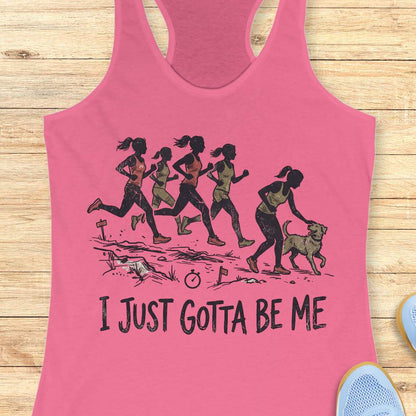 pink racerback tank top featuring a distressed vintage-style illustration of five runners on a trail. Four runners continue the race while one runner stops to pet a friendly dog beside the path. Small trail markers and a stopwatch appear in the scene. The design includes the phrase: “I JUST GOTTA BE ME.” The artwork uses muted coral, olive green, and black tones, celebrating runners who prioritize joy and dogs over competition.