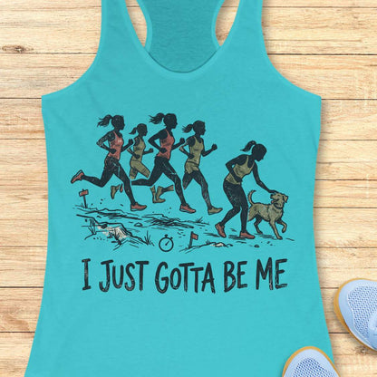 blue racerback tank top featuring a distressed vintage-style illustration of five runners on a trail. Four runners continue the race while one runner stops to pet a friendly dog beside the path. Small trail markers and a stopwatch appear in the scene. The design includes the phrase: “I JUST GOTTA BE ME.” The artwork uses muted coral, olive green, and black tones, celebrating runners who prioritize joy and dogs over competition.
