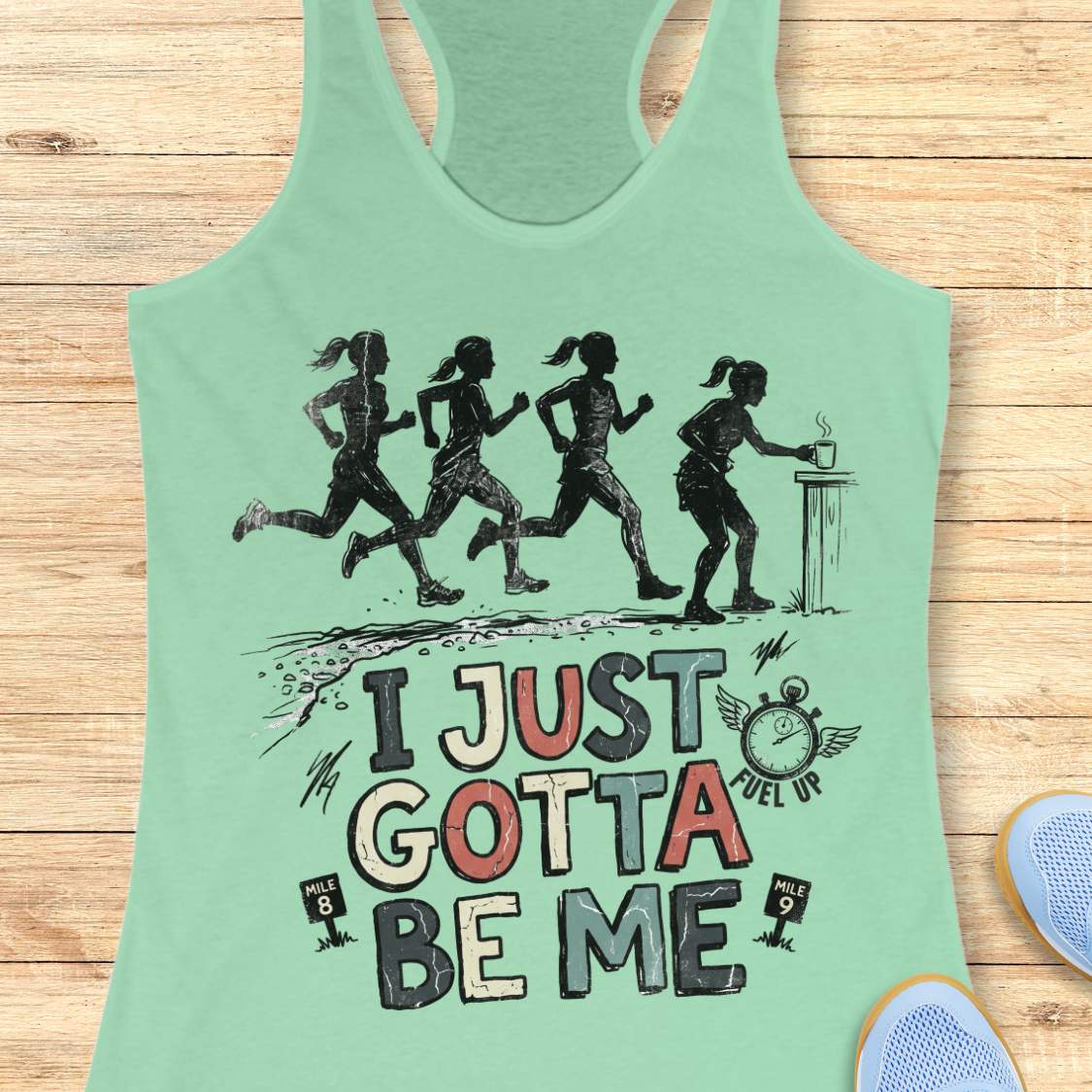 mint racerback tank top featuring a distressed vintage-style running design. Four runners move along a trail, while one runner pauses at a table to grab a steaming cup, suggesting a mid-run coffee or fuel stop. Below the illustration is the phrase “I JUST GOTTA BE ME” in large multicolored lettering, accompanied by a winged stopwatch labeled “Fuel Up” and mile markers reading “Mile 8” and “Mile 9.” The design celebrates runners who embrace their own pace and priorities, including stopping to refuel dur