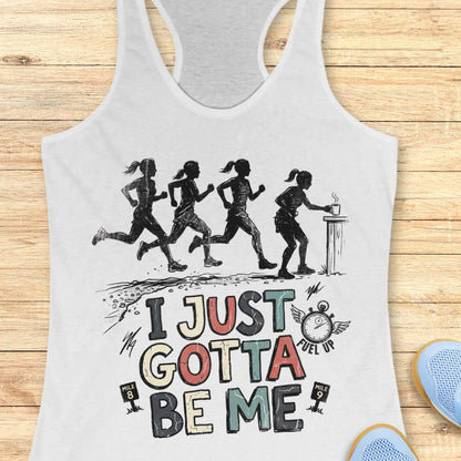 white racerback tank top featuring a distressed vintage-style running design. Four runners move along a trail, while one runner pauses at a table to grab a steaming cup, suggesting a mid-run coffee or fuel stop. Below the illustration is the phrase “I JUST GOTTA BE ME” in large multicolored lettering, accompanied by a winged stopwatch labeled “Fuel Up” and mile markers reading “Mile 8” and “Mile 9.” The design celebrates runners who embrace their own pace and priorities, including stopping to refuel dur