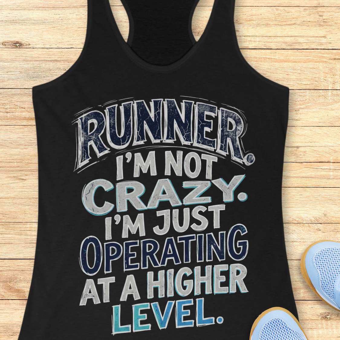Black racerback tank top featuring bold distressed typography in white, navy blue, and teal. The design displays the humorous runner slogan: “RUNNER. I’M NOT CRAZY. I’M JUST OPERATING AT A HIGHER LEVEL.” The statement is arranged in large stacked lettering with a vintage athletic style, combining confidence, humor, and runner pride. The design celebrates the unique mindset, dedication, and passion of the running community