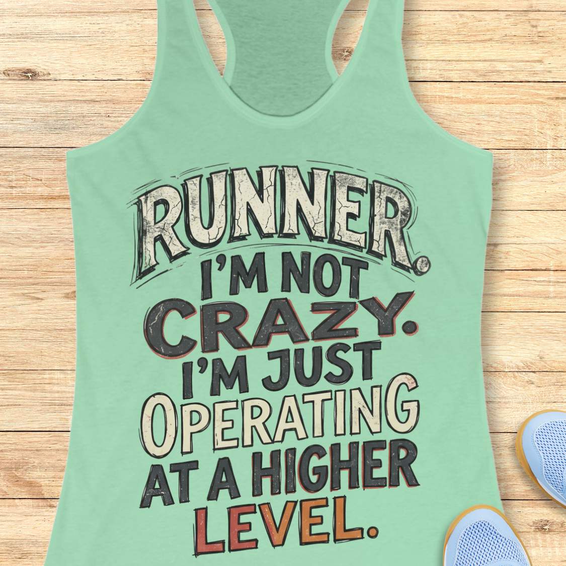 mint racerback tank top featuring bold distressed typography in white, navy blue, and teal. The design displays the humorous runner slogan: “RUNNER. I’M NOT CRAZY. I’M JUST OPERATING AT A HIGHER LEVEL.” The statement is arranged in large stacked lettering with a vintage athletic style, combining confidence, humor, and runner pride. The design celebrates the unique mindset, dedication, and passion of the running community