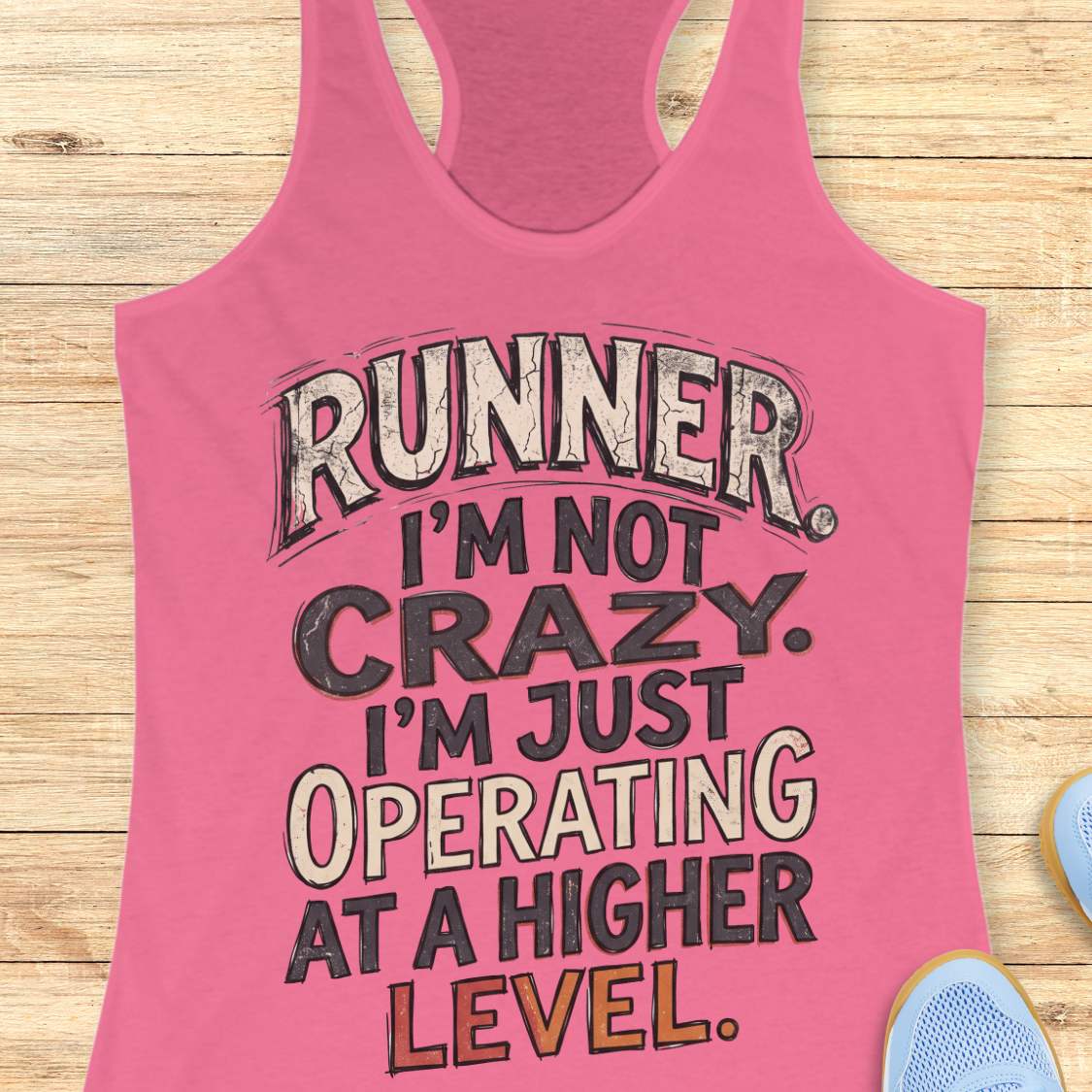 pink racerback tank top featuring bold distressed typography in white, navy blue, and teal. The design displays the humorous runner slogan: “RUNNER. I’M NOT CRAZY. I’M JUST OPERATING AT A HIGHER LEVEL.” The statement is arranged in large stacked lettering with a vintage athletic style, combining confidence, humor, and runner pride. The design celebrates the unique mindset, dedication, and passion of the running community