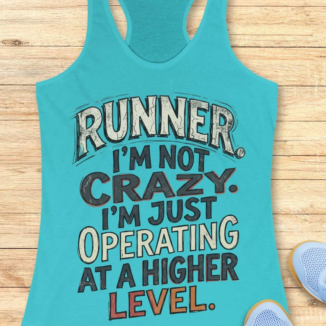 blue racerback tank top featuring bold distressed typography in white, navy blue, and teal. The design displays the humorous runner slogan: “RUNNER. I’M NOT CRAZY. I’M JUST OPERATING AT A HIGHER LEVEL.” The statement is arranged in large stacked lettering with a vintage athletic style, combining confidence, humor, and runner pride. The design celebrates the unique mindset, dedication, and passion of the running community