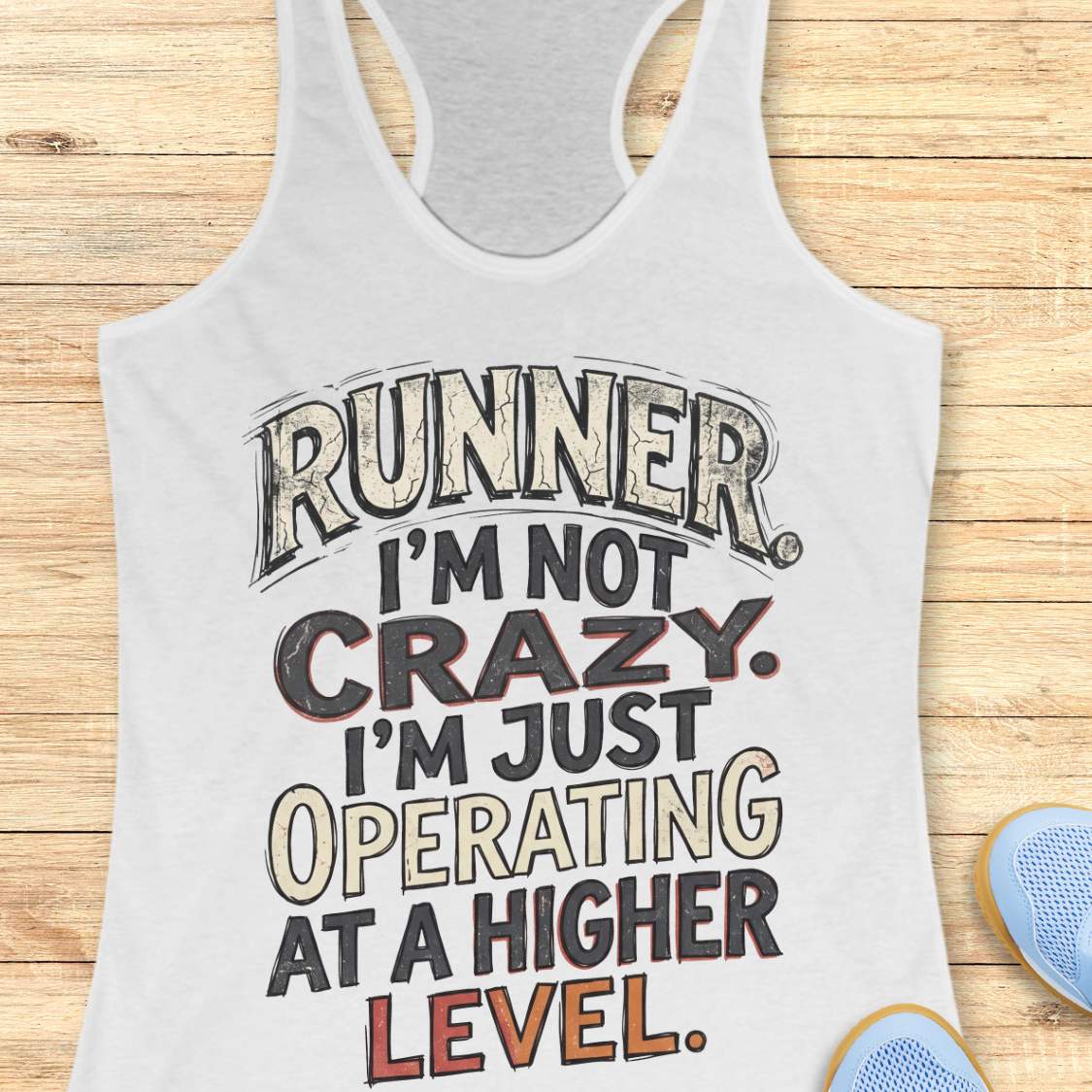 white racerback tank top featuring bold distressed typography in white, navy blue, and teal. The design displays the humorous runner slogan: “RUNNER. I’M NOT CRAZY. I’M JUST OPERATING AT A HIGHER LEVEL.” The statement is arranged in large stacked lettering with a vintage athletic style, combining confidence, humor, and runner pride. The design celebrates the unique mindset, dedication, and passion of the running community