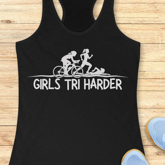 Black racerback tank top featuring a clean white graphic celebrating triathlon athletes. The design shows three silhouettes representing the sports of a triathlon: a cyclist riding a bicycle, a runner in motion, and a swimmer moving through the water. Beneath the illustration, bold lettering reads “GIRLS TRI HARDER.” The minimalist design combines athletic pride, determination, and humor, making it a fun statement piece for women who participate in triathlons and endurance sports.