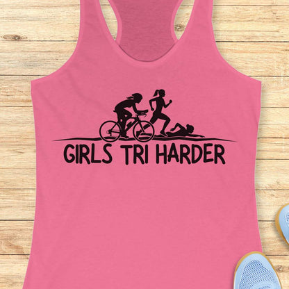 pink racerback tank top featuring a clean white graphic celebrating triathlon athletes. The design shows three silhouettes representing the sports of a triathlon: a cyclist riding a bicycle, a runner in motion, and a swimmer moving through the water. Beneath the illustration, bold lettering reads “GIRLS TRI HARDER.” The minimalist design combines athletic pride, determination, and humor, making it a fun statement piece for women who participate in triathlons and endurance sports.