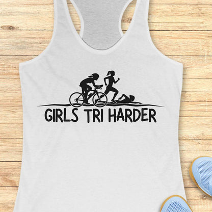 white racerback tank top featuring a clean white graphic celebrating triathlon athletes. The design shows three silhouettes representing the sports of a triathlon: a cyclist riding a bicycle, a runner in motion, and a swimmer moving through the water. Beneath the illustration, bold lettering reads “GIRLS TRI HARDER.” The minimalist design combines athletic pride, determination, and humor, making it a fun statement piece for women who participate in triathlons and endurance sports.