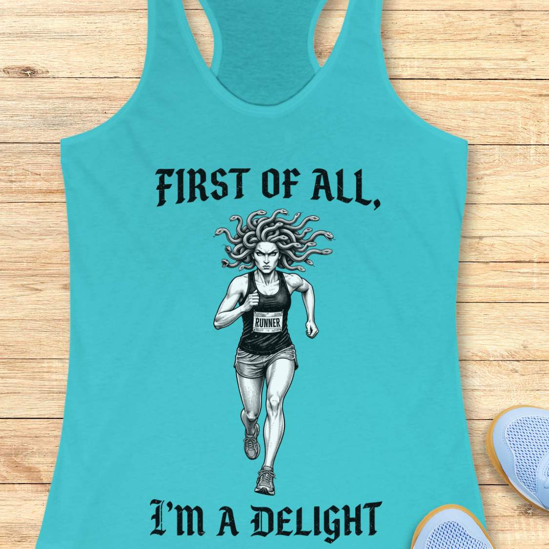 Turquoise women's racerback running tank top displayed on a light wood surface. The design features a black-and-white illustration of a runner with Medusa-style snake hair wearing a race bib. Above the runner, gothic-style text reads “FIRST OF ALL,” and below the runner, matching text reads “I’M A DELIGHT.” Running shoes are partially visible in the corners of the image.