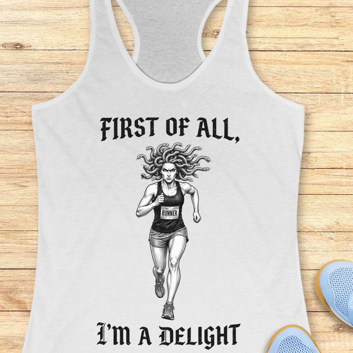 white women's racerback running tank top displayed on a light wood surface. The design features a black-and-white illustration of a runner with Medusa-style snake hair wearing a race bib. Above the runner, gothic-style text reads “FIRST OF ALL,” and below the runner, matching text reads “I’M A DELIGHT.” Running shoes are partially visible in the corners of the image.