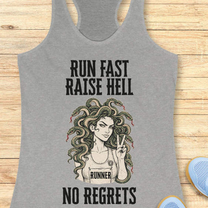 grey racerback tank top for women displayed on a light wood background. The design features bold vintage-style text reading “RUN FAST RAISE HELL” at the top and “NO REGRETS” at the bottom. In the center is an illustration of a runner with Medusa-inspired snake hair, wearing a race bib labeled “RUNNER” and holding up a peace sign. Partial running shoes are visible in the lower corners of the image.