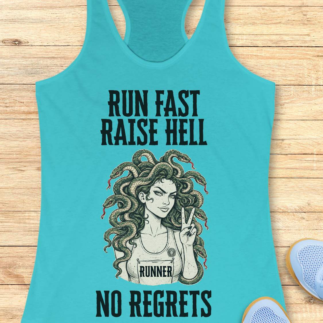 blue racerback tank top for women displayed on a light wood background. The design features bold vintage-style text reading “RUN FAST RAISE HELL” at the top and “NO REGRETS” at the bottom. In the center is an illustration of a runner with Medusa-inspired snake hair, wearing a race bib labeled “RUNNER” and holding up a peace sign. Partial running shoes are visible in the lower corners of the image.