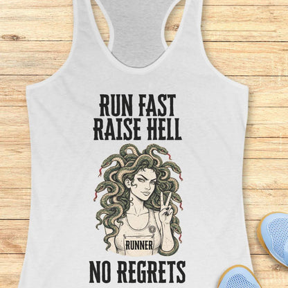 white racerback tank top for women displayed on a light wood background. The design features bold vintage-style text reading “RUN FAST RAISE HELL” at the top and “NO REGRETS” at the bottom. In the center is an illustration of a runner with Medusa-inspired snake hair, wearing a race bib labeled “RUNNER” and holding up a peace sign. Partial running shoes are visible in the lower corners of the image.