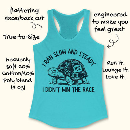 Turquoise women's racerback running tank top displayed on a light wood background. The design features a black illustrated tortoise wearing a race bib numbered “102.” Curved text above the tortoise reads “I RAN SLOW AND STEADY,” and text below reads “I DIDN’T WIN THE RACE.” Partial running shoes are visible in the lower corners of the image.