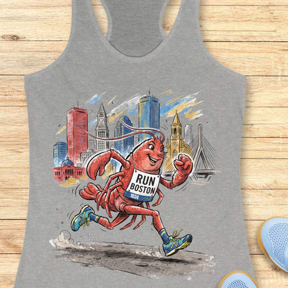 A heather gray racerback tank top featuring a colorful graphic of a cartoon lobster running with a 'RUN BOSTON 2025' bib, set against a stylized Boston skyline. The tank top is displayed flat on a light wood plank background.