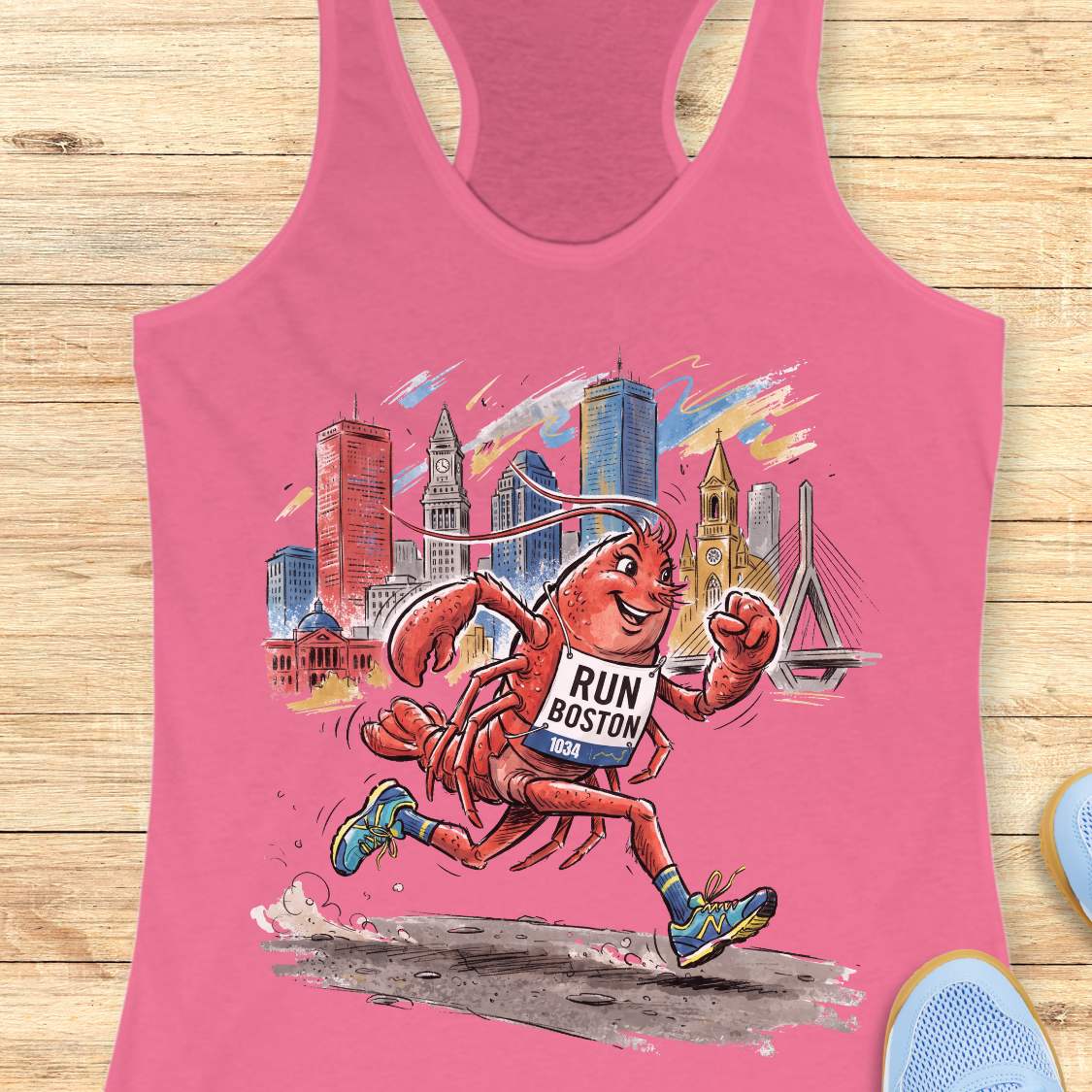 A pink racerback tank top laid flat on a light wood surface, featuring a colorful graphic of a lobster running with a 'RUN BOSTON' bib and a city skyline in the background.