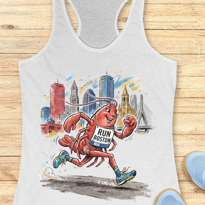 A white racerback tank top laid flat on a light wood surface, featuring a colorful graphic of a running lobster in front of a city skyline with the text 'RUN BOSTON 2024'. Partial blue shoes are visible at the bottom right edge.