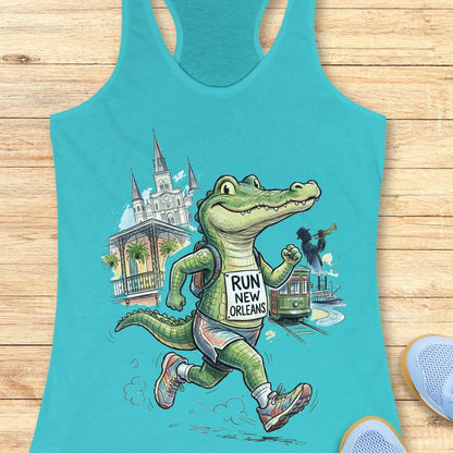 A turquoise racerback tank top laid flat on a light wood surface, featuring a colorful cartoon alligator running with a backpack that reads 'RUN NEW ORLEANS.' Partial blue sneakers are visible at the bottom right as styling props.