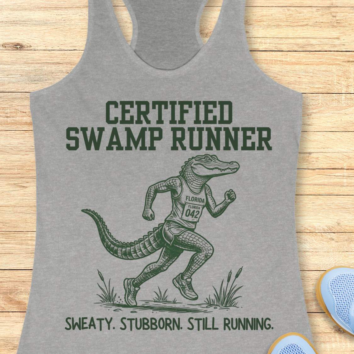 Funny swamp runner grey tank top featuring a running alligator wearing a race bib and athletic gear with the slogan “Certified Swamp Runner: Sweaty. Stubborn. Still Running.” Perfect for women runners, Florida runners, trail runners, marathon training, and runners who embrace hot, humid miles.
