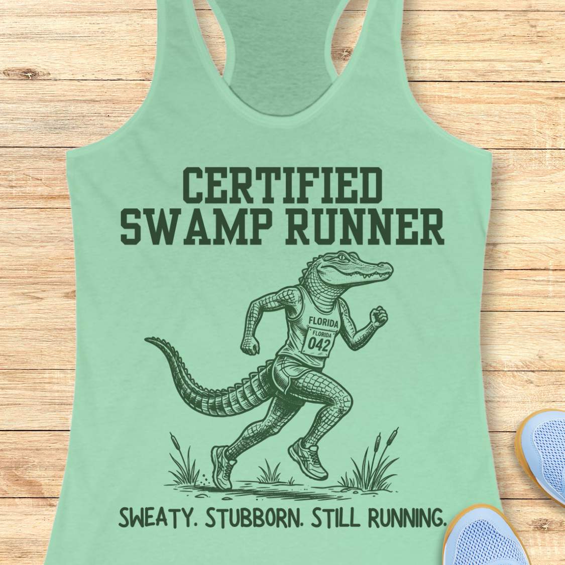 Funny swamp runner mint tank top featuring a running alligator wearing a race bib and athletic gear with the slogan “Certified Swamp Runner: Sweaty. Stubborn. Still Running.” Perfect for women runners, Florida runners, trail runners, marathon training, and runners who embrace hot, humid miles.