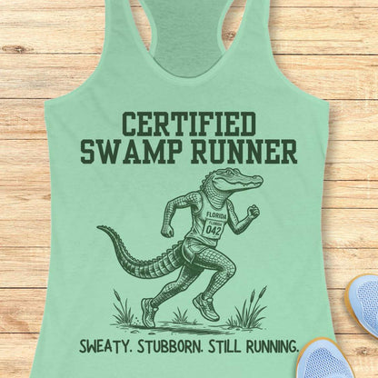 Funny swamp runner mint tank top featuring a running alligator wearing a race bib and athletic gear with the slogan “Certified Swamp Runner: Sweaty. Stubborn. Still Running.” Perfect for women runners, Florida runners, trail runners, marathon training, and runners who embrace hot, humid miles.