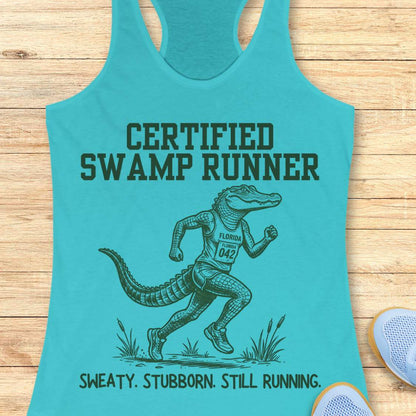 Funny swamp runner blue tank top featuring a running alligator wearing a race bib and athletic gear with the slogan “Certified Swamp Runner: Sweaty. Stubborn. Still Running.” Perfect for women runners, Florida runners, trail runners, marathon training, and runners who embrace hot, humid miles.