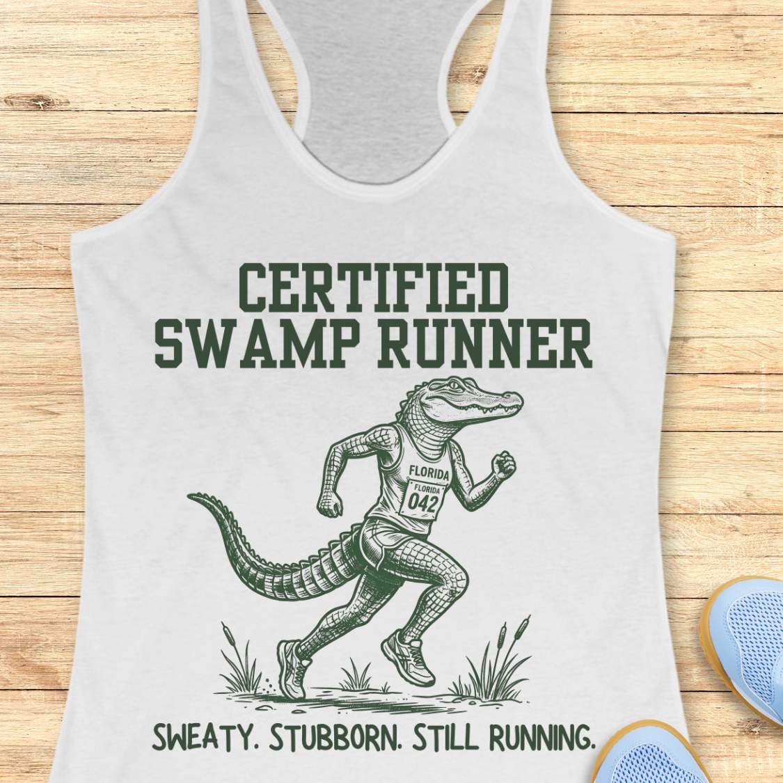 Funny swamp runner white tank top featuring a running alligator wearing a race bib and athletic gear with the slogan “Certified Swamp Runner: Sweaty. Stubborn. Still Running.” Perfect for women runners, Florida runners, trail runners, marathon training, and runners who embrace hot, humid miles.