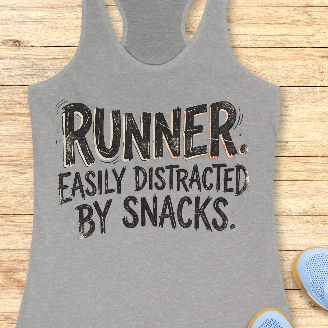 Funny runner tank top featuring the bold phrase “RUNNER. EASILY DISTRACTED BY SNACKS.” in distressed white typography on a grey racerback tank. Humorous running apparel for women who love running, carbs, post-run treats, energy gels, race snacks, and recovery food. Perfect for runners who are motivated by snacks, distracted by aid stations, and always thinking about their next treat after a run. Fun running gift for women runners, marathon runners, half marathon runners, 5K runners, trail runners, running 