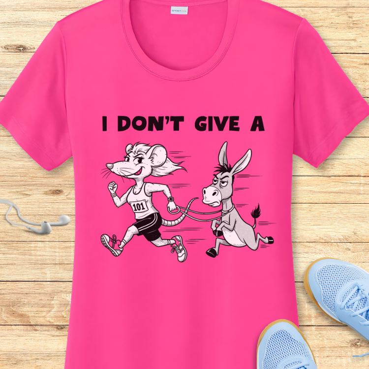 Graphic print on a hot pink t-shirt featuring a cartoon mouse with a 101 bib running and pulling a grumpy donkey on a leash, with the text I DON'T GIVE A above, displayed on a wooden surface with blue sneakers and white earbuds nearby