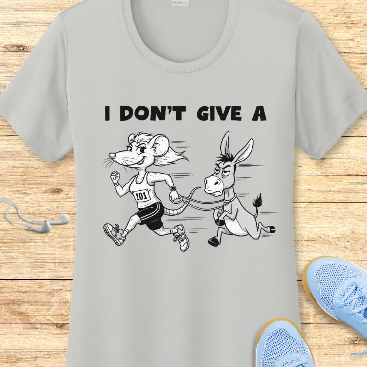 Light gray t-shirt featuring a cartoon of a smiling mouse runner with bib 101 pulling a grumpy donkey on a leash, beneath the text I DON'T GIVE A, shown on a wooden background with light blue sneakers