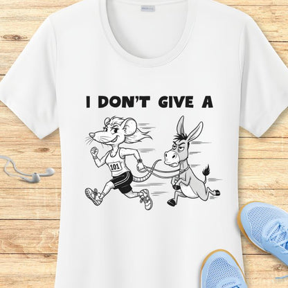 White t-shirt displaying a cartoon graphic of a determined mouse runner with bib 101 pulling a grumpy donkey on a leash, and the text 'I DON'T GIVE A' above, presented on a wooden background with visible blue running shoes and white earbuds