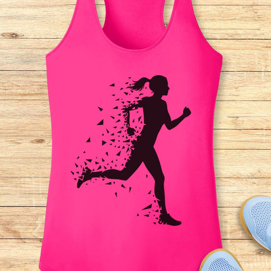 A bright pink racerback tank top with a black silhouette of a running woman who appears to be breaking apart into small fragments, laid flat on a light wood plank background with partial shoes visible at the edges.