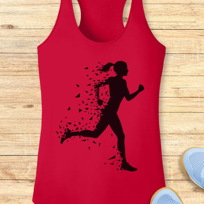 A red racerback tank top with a black silhouette graphic of a running woman whose body dissolves into small fragments, displayed flat on a light wood plank background with partial sneakers visible at the edges.